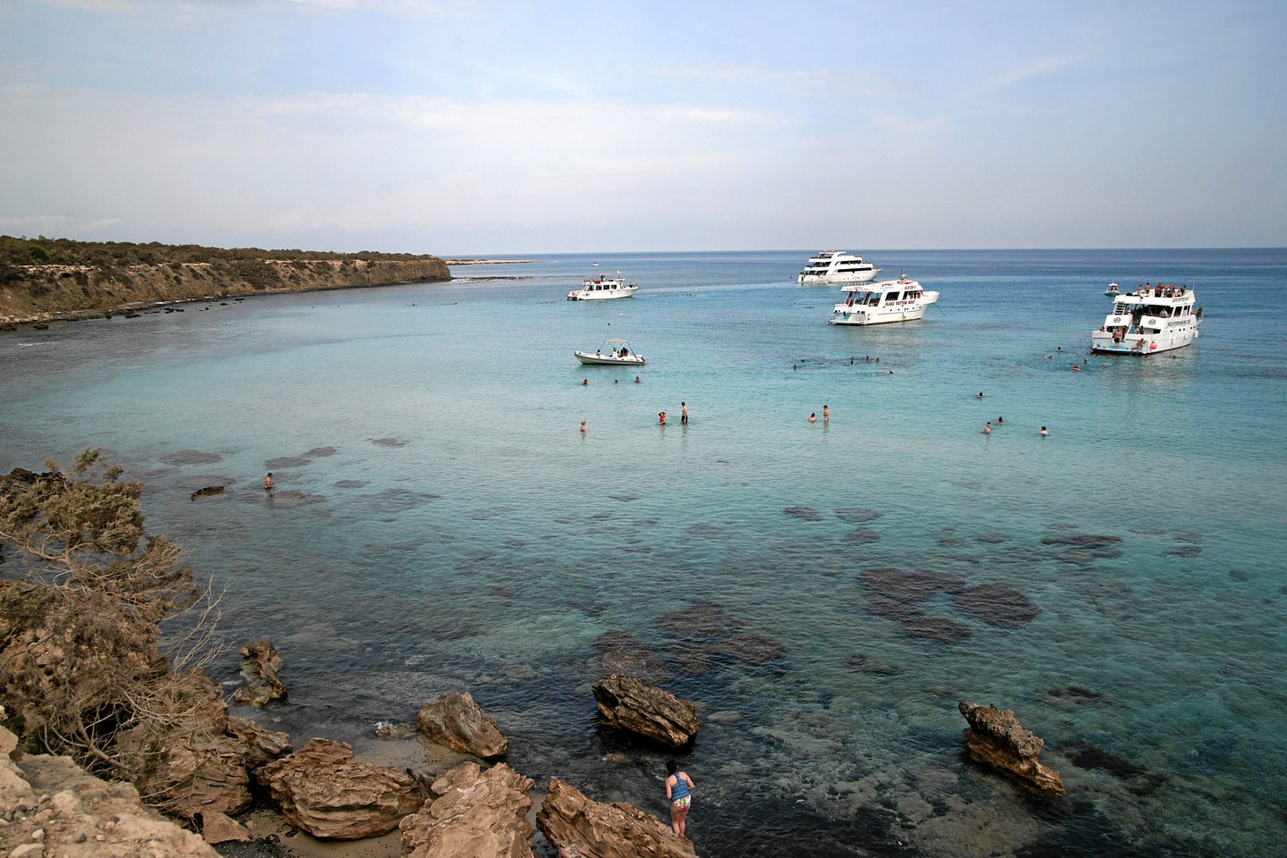 Boats moored on the clear turquoise water of the Blue Lagoon below the low Akamas cliffs
