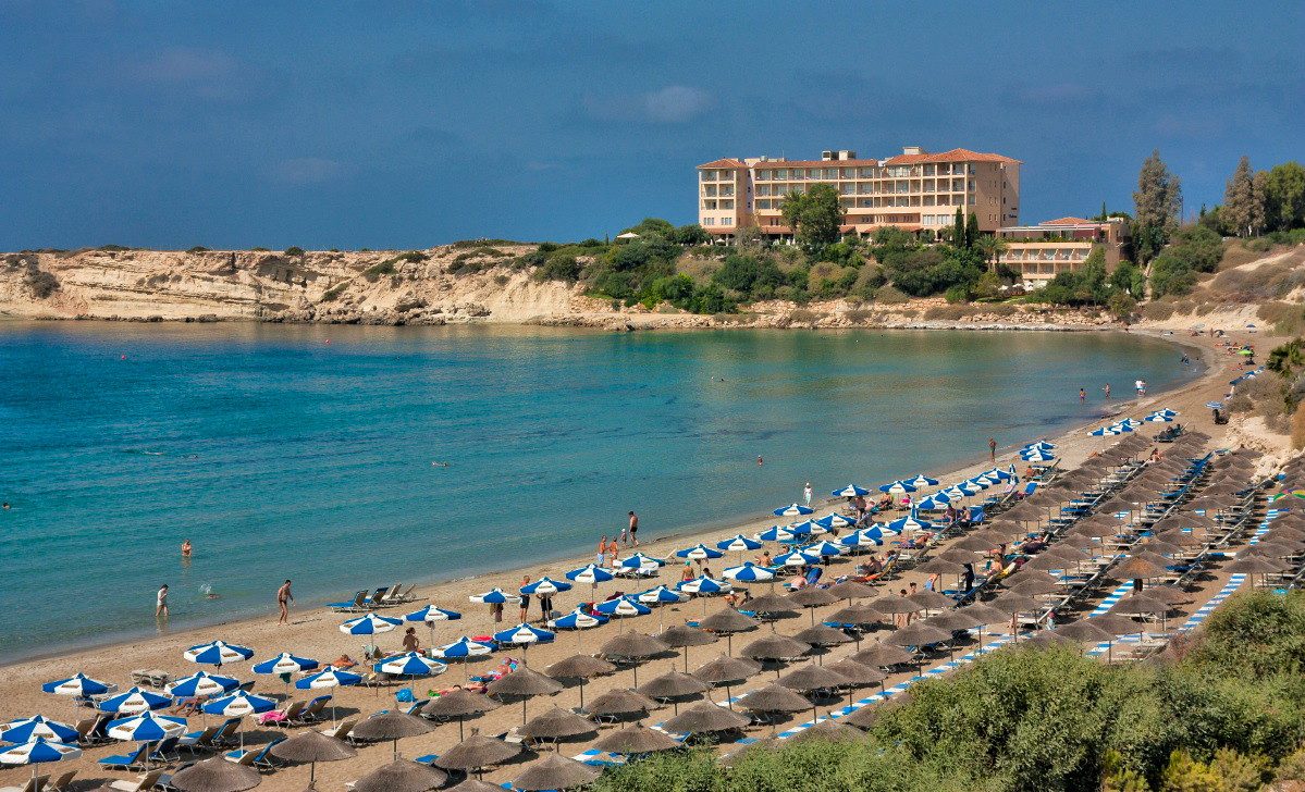 Sheltered crescent of sand at Coral Bay lined with parasols below the headland hotel