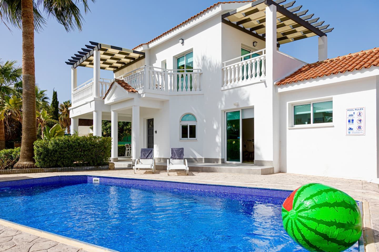 Whitewashed villa with pergola balconies rising behind the full length of the private pool
