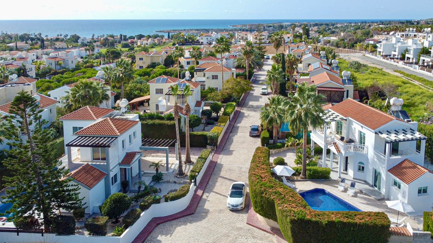 Aerial view across Coral Bay rooftops and palm trees to the blue Mediterranean horizon
